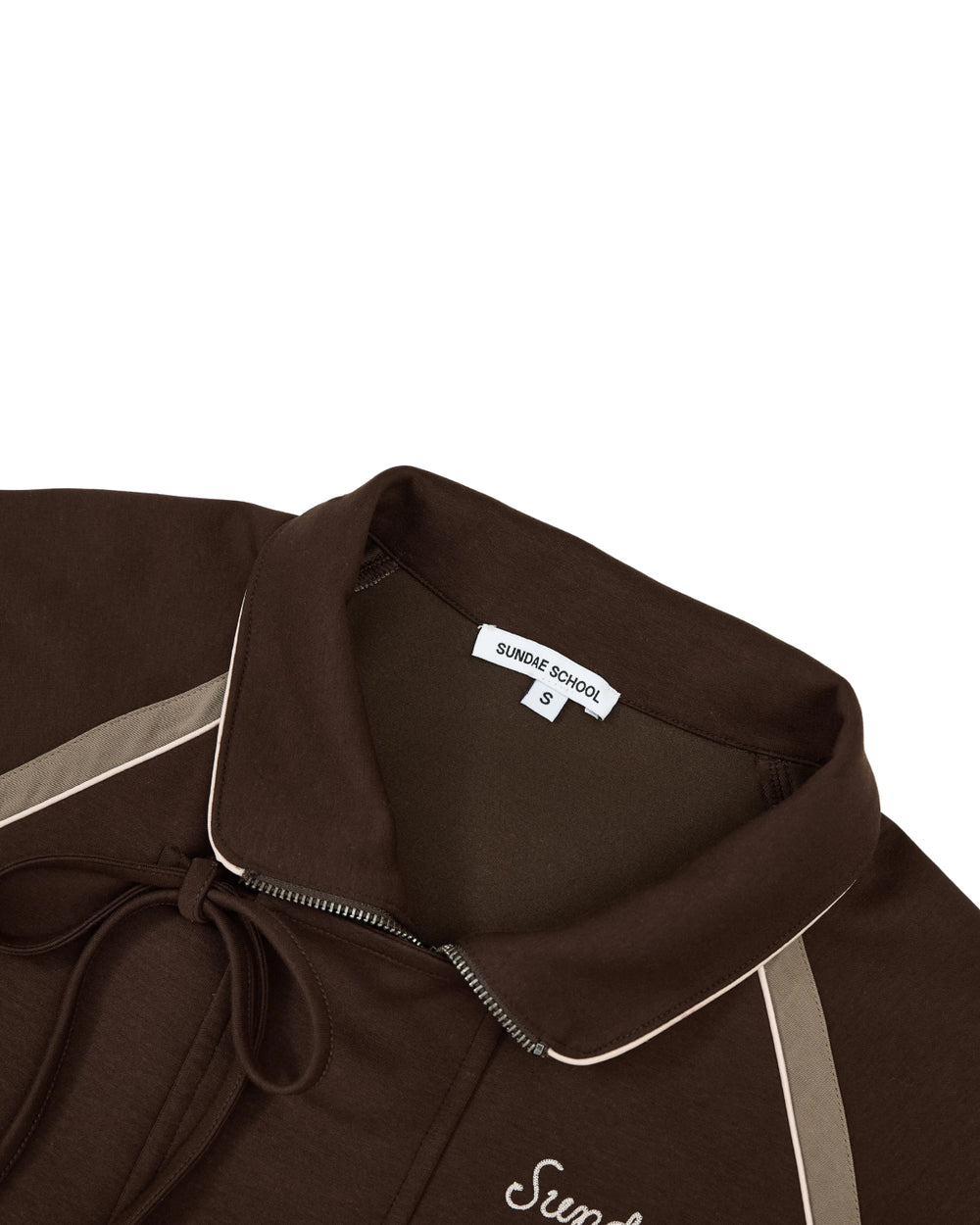 Close-up of the Sundae School BROWN PALISADE PARK TRACK JACKET, featuring a brown zip-up design with a collared neckline, beige piping, and drawstring details. A visible white label reading Sundae School S appears inside the neckline. Subtle contrast fabric accents along the edges lend an elevated finish reminiscent of an athletic track jacket—all displayed on a plain white background.