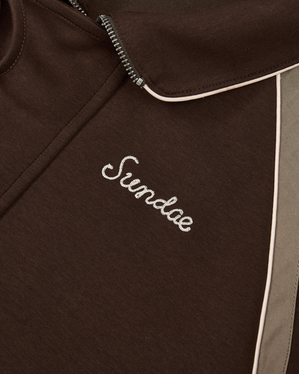 Close-up of the Sundae School Brown Palisade Park Track Jacket featuring contrast fabric light trim and “Sundae” embroidered in white cursive chain-stitch on the chest.