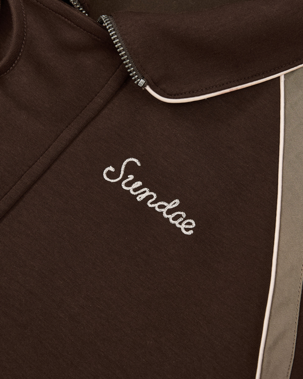 Close-up of the Sundae School Brown Palisade Park Track Jacket featuring contrast fabric light trim and “Sundae” embroidered in white cursive chain-stitch on the chest.