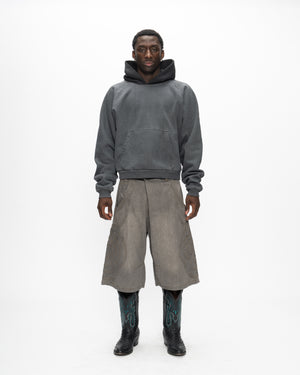 A person stands against a white background wearing Sundae School’s GREY JORTS JOONIVERSE and a dark gray hoodie, paired with black cowboy boots featuring turquoise details.