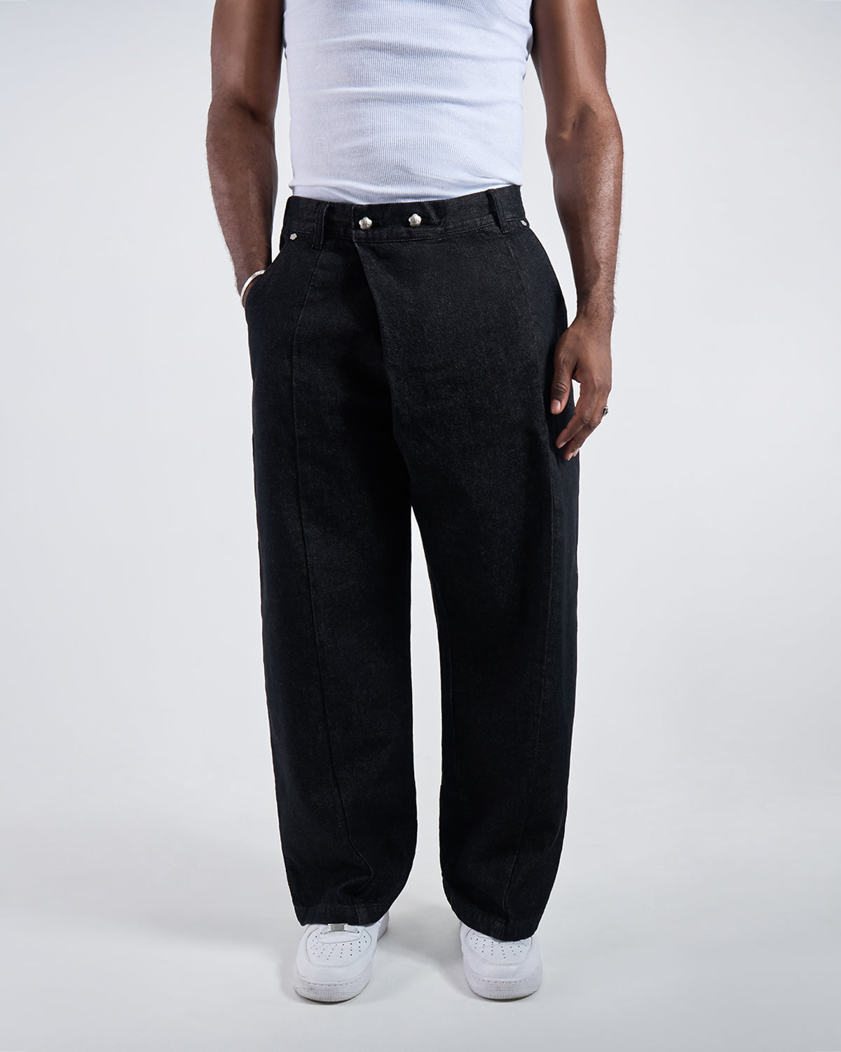 Black wide-leg hanbok denim pants modeled with white ribbed tank top, front view showing asymmetric closure with silver flower snap buttons, relaxed fit silhouette against white studio background