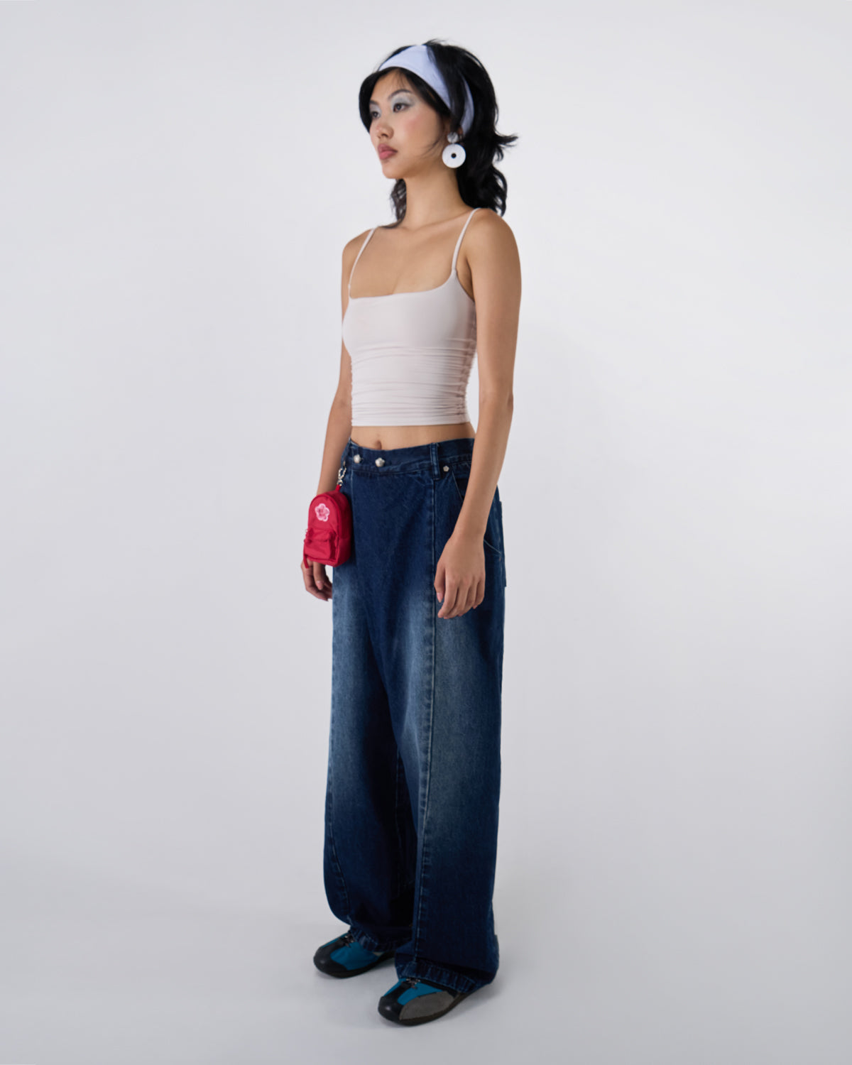 Side profile view of indigo fade wide-leg hanbok denim pants modeled with white ruched bandeau top, white headband and disc earrings, red mini backpack charm, demonstrating relaxed fit silhouette against white studio background