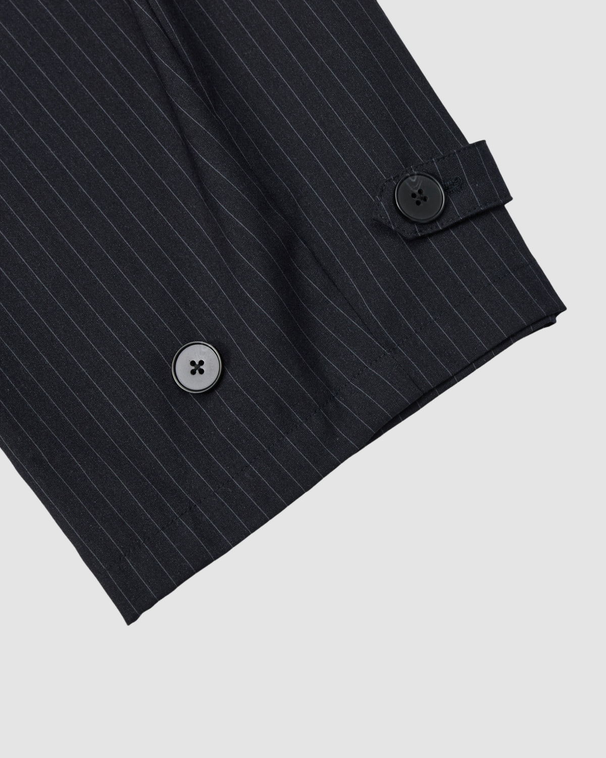 Close-up of Sundae School's KIKI DRAWSTRING SLACKS in black pinstripe: the sleeve features two black buttons and a buttoned strap detail, echoing the tailored yet relaxed design with a barrel leg and elastic drawstring waist, on a light gray background.