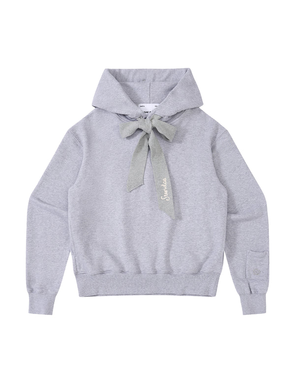The HEATHER GREY KNIT TIE HOODIE by Sundae School is a light gray, heavyweight sweatshirt featuring a large knit bow at the neck, long sleeves, and ribbed cuffs and hem. Made from soft brushed cotton for extra comfort, this unisex hoodie is finished with “Salut” embroidered in cursive near the bow.