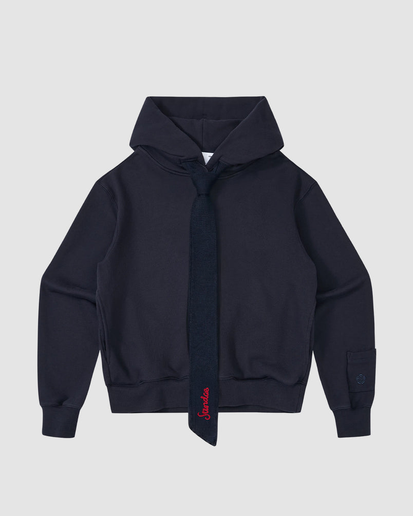 The NAVY KNIT TIE HOODIE by Sundae School is a heavyweight brushed cotton hoodie in navy, featuring a matching knit tie with red embroidery, ribbed cuffs and waistband, shown against a light gray background.