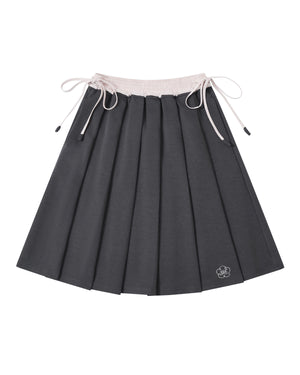 The CHARCOAL KONA MIDI SKIRT by Sundae School is a dark gray pleated skirt featuring a light pink drawstring waistband and a small embroidered bear face near the hem.