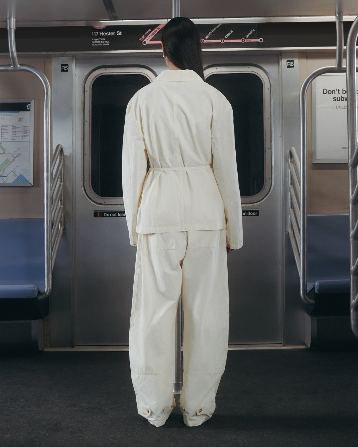Clad in Sundae School’s IVORY LINEN GORUM BLAZER, a person stands inside an empty subway car, back to the camera and facing the train doors.