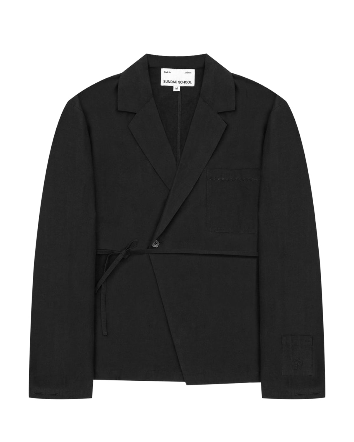 The Sundae School BLACK LINEN GORUM BLAZER is an unstructured black wrap-style blazer featuring a single button, left chest pocket, and a tie closure at the waist, displayed against a white background.