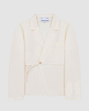 The IVORY LINEN GORUM BLAZER by Sundae School is a cream-colored, single-breasted blazer featuring a notched lapel, front button closure, waist tie, and chest pocket, displayed against a plain light background.