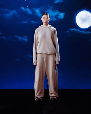 A person wearing the TAUPE WRAP SWEATBAJI by Sundae School stands against a dark blue night sky filled with clouds and a bright full moon.