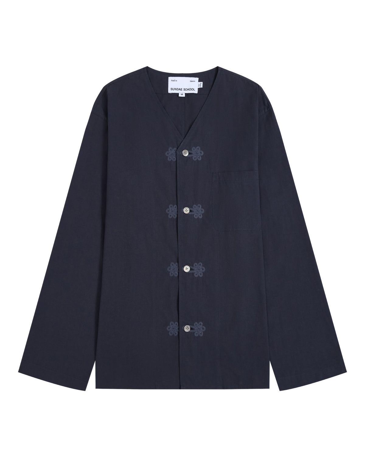 The MAEHWA COLLARLESS SHIRT by Sundae School is a navy blue, long-sleeve mid-layer featuring a V-neck, frog closures, and a single chest pocket. This versatile unisex piece is displayed laid flat on a white background.