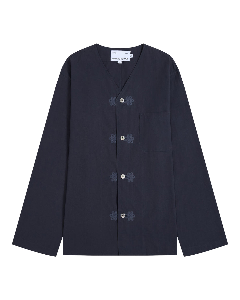 The MAEHWA COLLARLESS SHIRT by Sundae School is a navy blue, long-sleeve mid-layer featuring a V-neck, frog closures, and a single chest pocket. This versatile unisex piece is displayed laid flat on a white background.