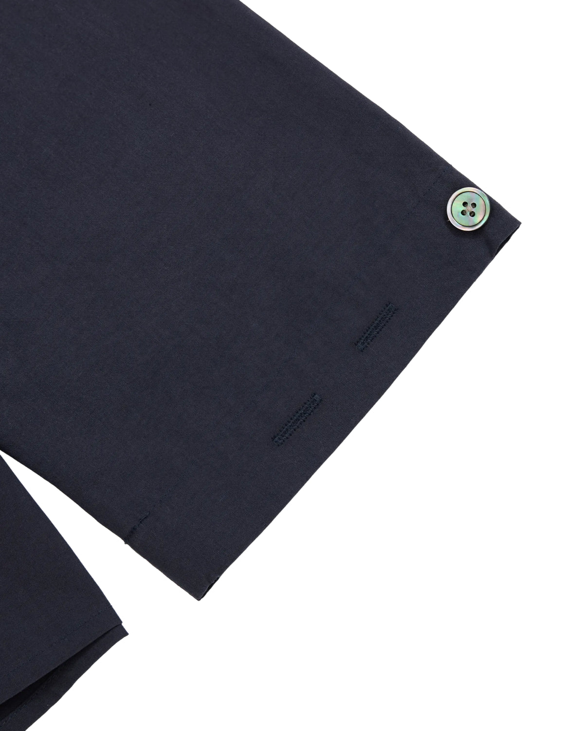 Close-up of a navy blue MAEHWA COLLARLESS SHIRT by Sundae School, highlighting its collarless linen cuff with a single greenish button and two unused buttonholes, isolated on a white background. This unisex mid-layer embodies minimal detailing and understated elegance.