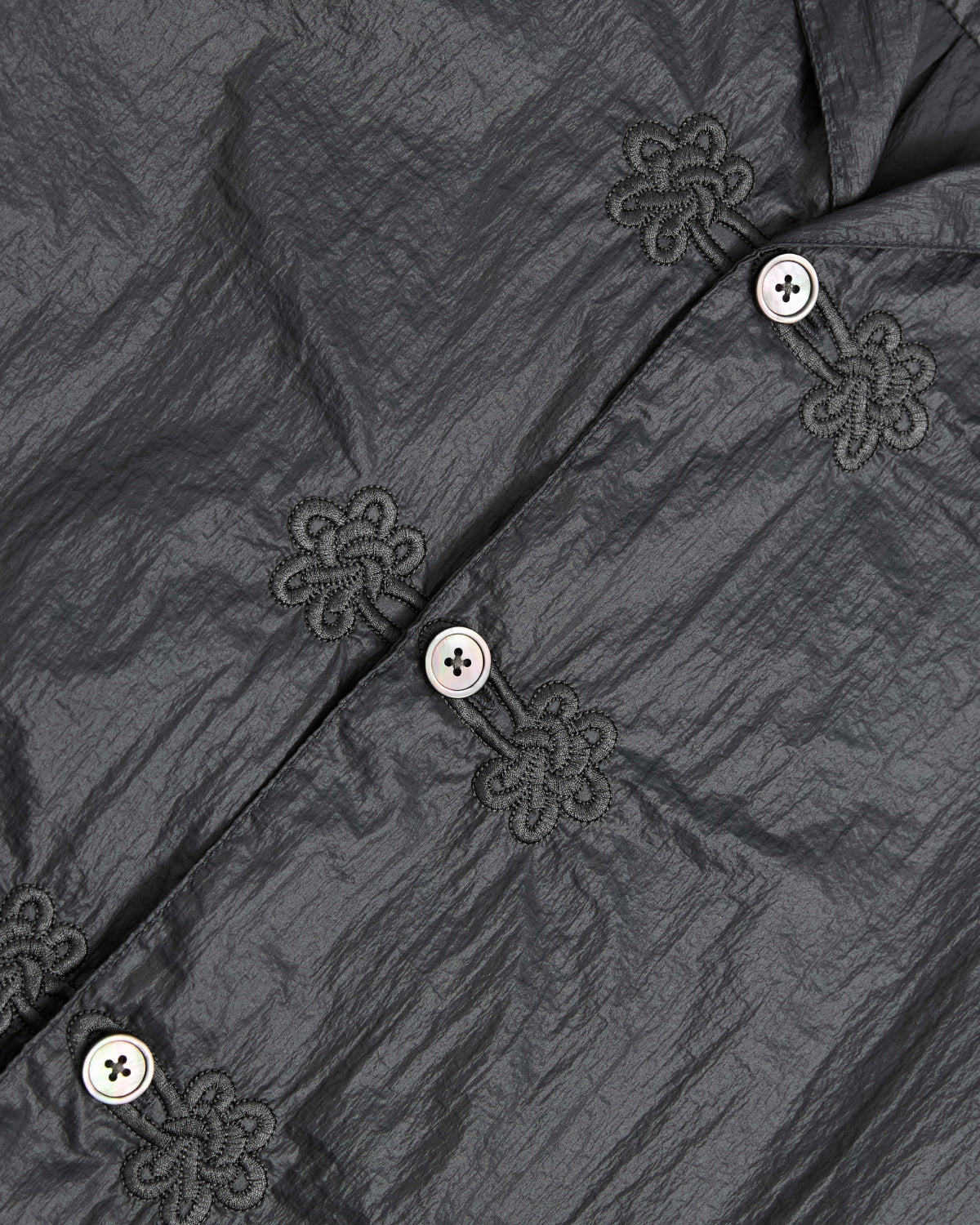 Close-up of the Sundae School MAEHWA EMBROIDERED SHEER SHIRT in crinkled dark gray nylon, featuring white buttons with decorative Maehwa embroidery around each buttonhole—an ideal unisex going-out shirt.