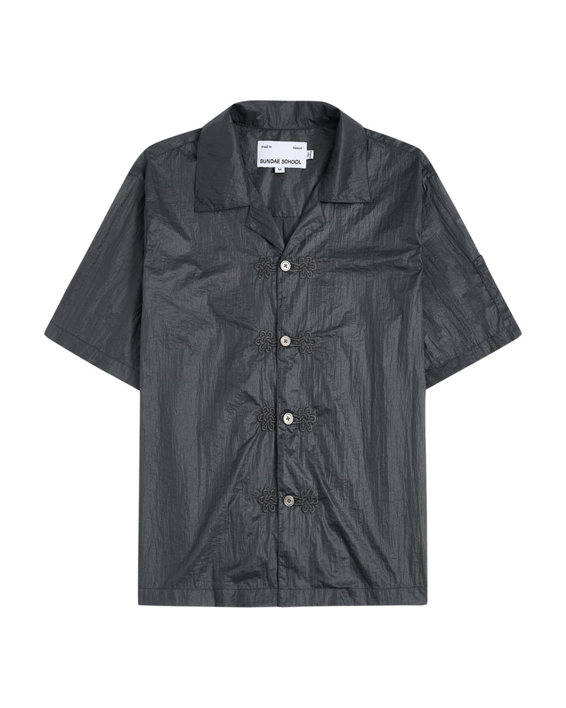 The MAEHWA EMBROIDERED SHEER SHIRT by Sundae School is a short-sleeve, dark gray, collared button-up featuring a crinkled texture and distinctive flower-shaped black buttons down the front—this unisex going-out shirt effortlessly elevates any look with its unique edge.