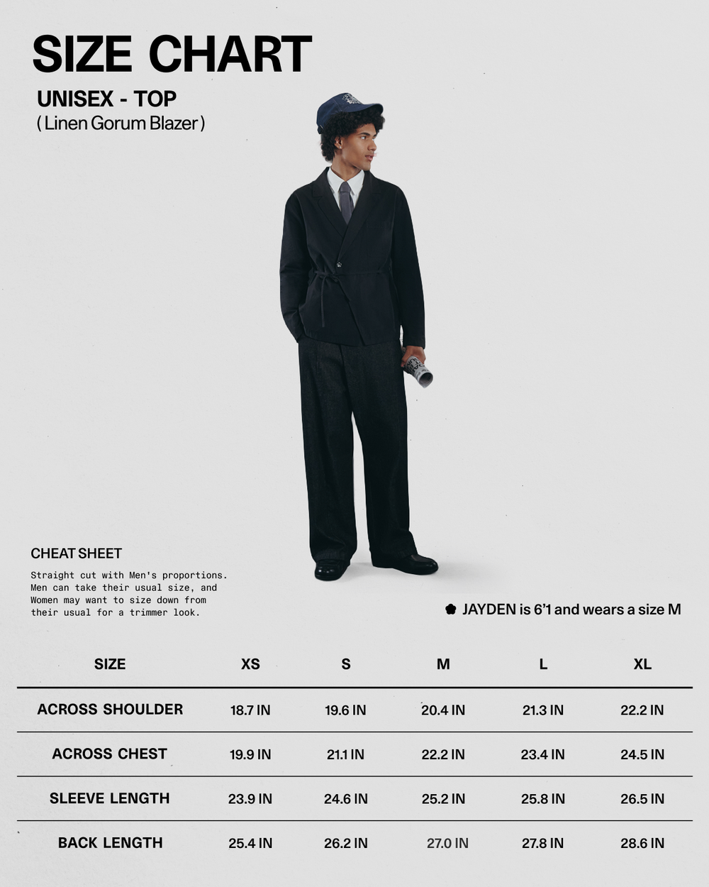 A person dressed in the BLACK LINEN GORUM BLAZER and black pants from Sundae School, paired with a blue hat, holds a rolled-up magazine. Below is a size chart for this unisex linen blazer by Sundae School, available in sizes XS to XL with measurements listed in inches.
