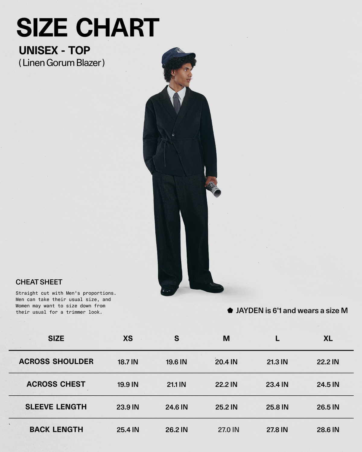 A person dressed in the BLACK LINEN GORUM BLAZER and black pants from Sundae School, paired with a blue hat, holds a rolled-up magazine. Below is a size chart for this unisex linen blazer by Sundae School, available in sizes XS to XL with measurements listed in inches.