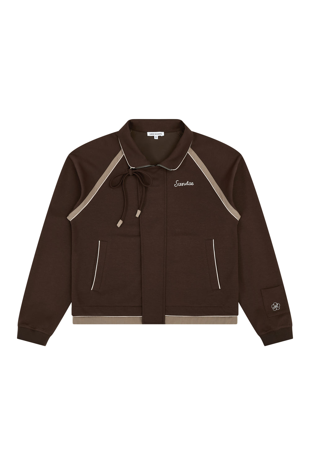 The BROWN PALISADE PARK TRACK JACKET by Sundae School is a brown zip-up athletic jacket featuring beige contrast fabric trim, front pockets, and a small embroidered logo on the left chest. It includes a collar with a tie and detailed chain-stitch embroidery on a patch near the left sleeve cuff.