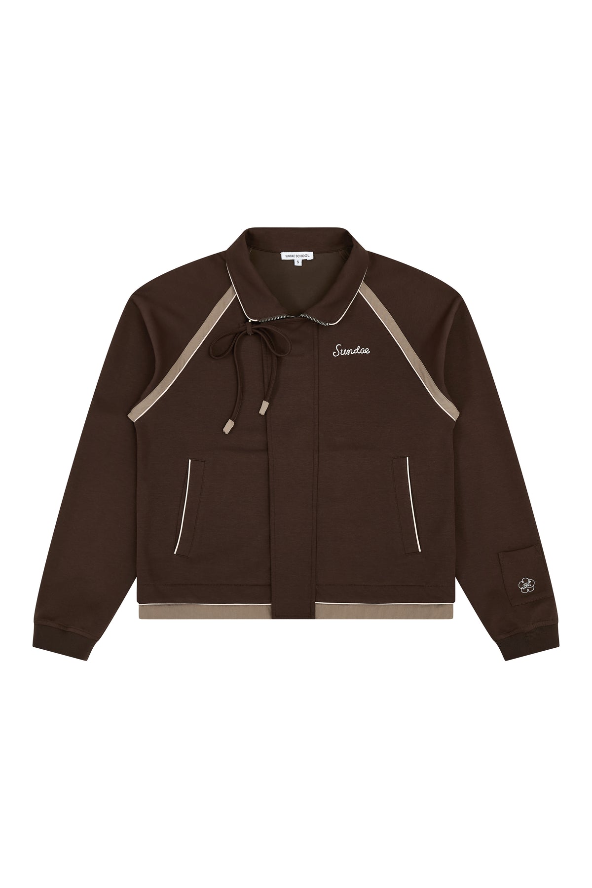 The BROWN PALISADE PARK TRACK JACKET by Sundae School is a brown zip-up athletic jacket featuring beige contrast fabric trim, front pockets, and a small embroidered logo on the left chest. It includes a collar with a tie and detailed chain-stitch embroidery on a patch near the left sleeve cuff.