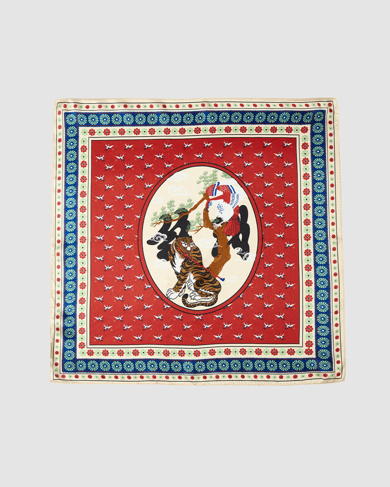 The MINHWA BANDANA by Sundae School is a square silk scarf inspired by Korean folk art, with a red background, ornate borders, and an oval center showing two women in traditional attire amid floral and geometric patterns—a unique luxury gift.
