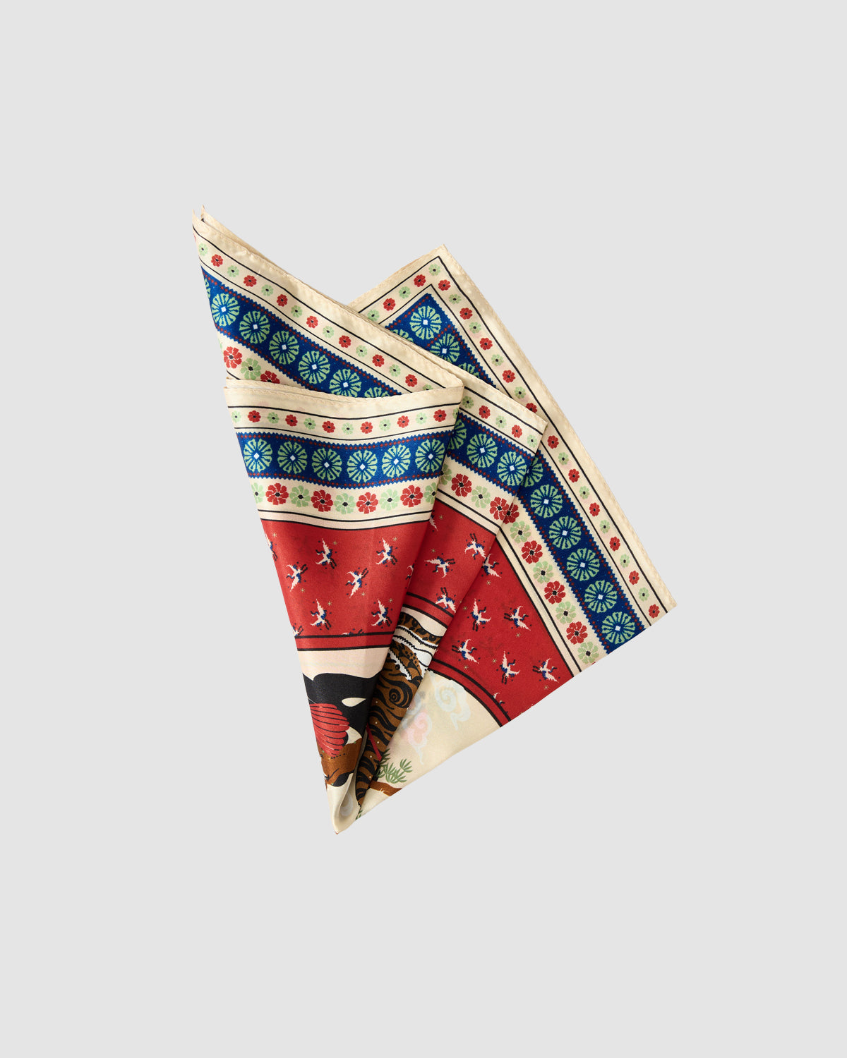 The MINHWA BANDANA by Sundae School is a silk scarf featuring a vibrant pattern of red, blue, beige, and black inspired by Korean folk art florals and geometric shapes, shown folded on a plain light gray background.