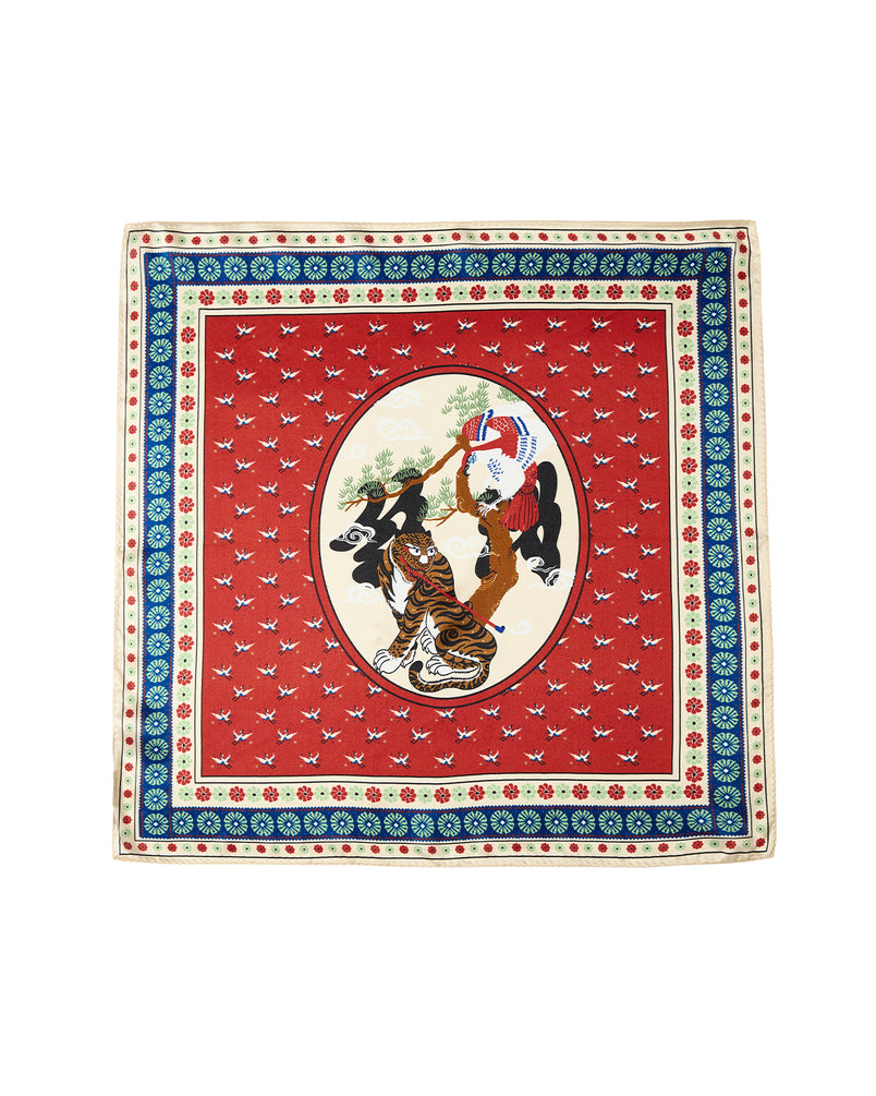 Experience the narrative artistry of the MINHWA BANDANA by Sundae School. Crafted from silk, this Korean folk art scarf features a vivid red background accented with an ornate blue and cream border, while its oval center portrays two women in traditional attire beneath a tree. Delicate bird motifs are scattered throughout, making this luxury accessory an ideal gift to elevate any collection.