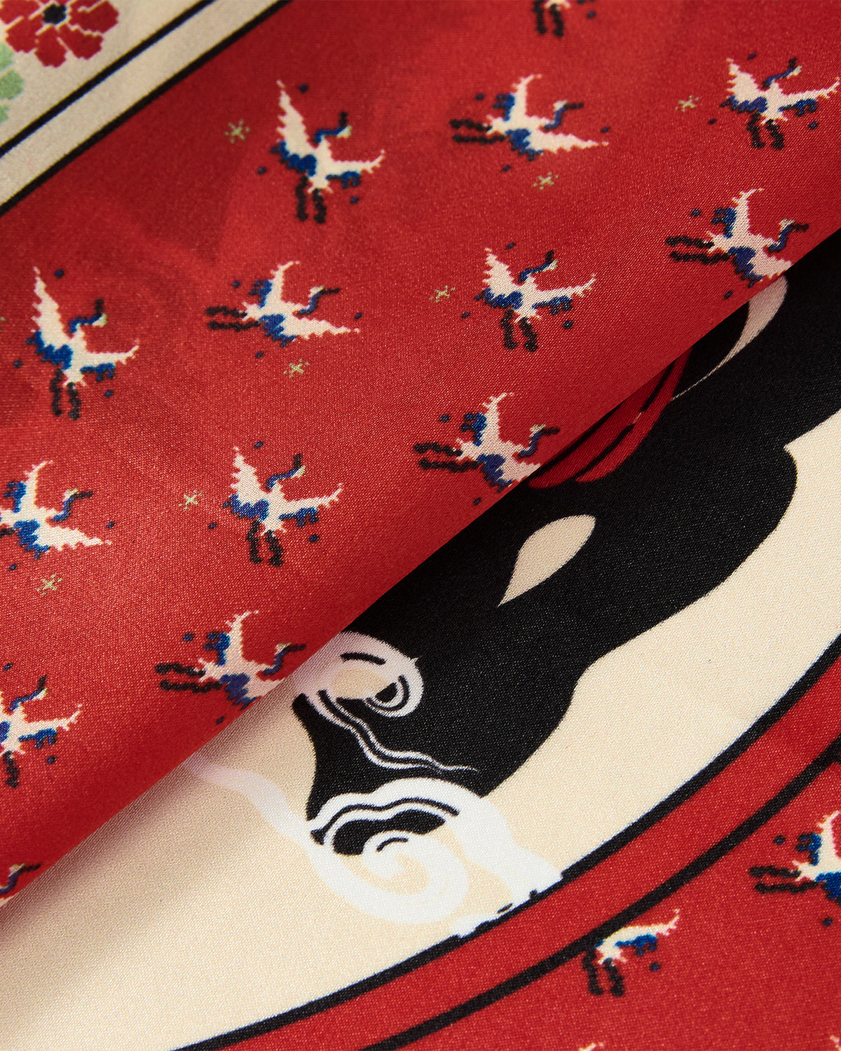 A close-up of red fabric featuring a pattern of small white and blue birds alongside a partially visible black and white design on a lighter background, the MINHWA BANDANA by Sundae School is a narrative-driven silk masterpiece—perfect as a luxury gift.