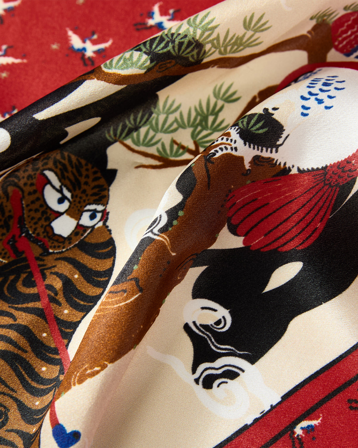 A close-up of the vibrant MINHWA BANDANA by Sundae School, a silk Korean folk art scarf adorned with a tiger, tree branches, and a red-crowned crane in an Asian-inspired design; bold lines and rich colors tell a captivating story—making this luxury piece an exquisite gift.
