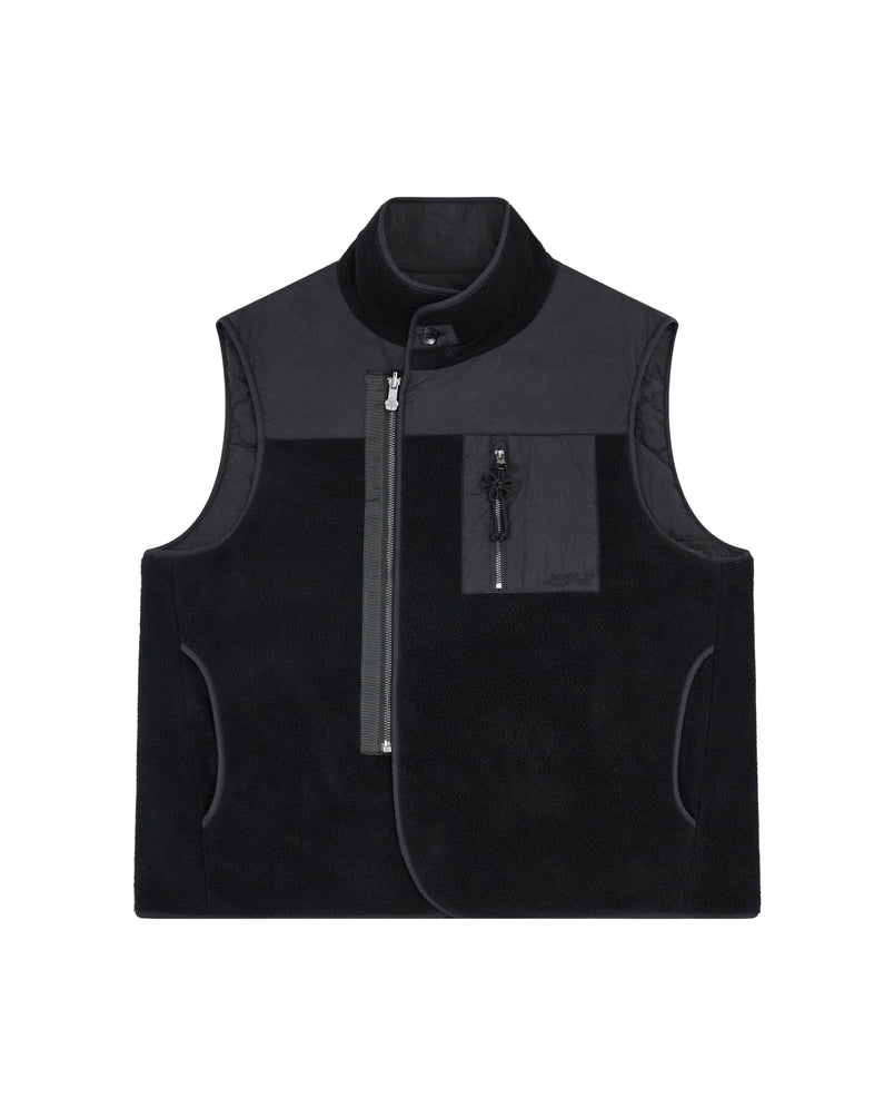The BLACK MOMO REVERSIBLE FLEECE VEST by Sundae School is a sleeveless, black fleece vest featuring a high collar, asymmetrical front zipper, zippered chest pocket, and side pockets. The vest is displayed flat on a white background.