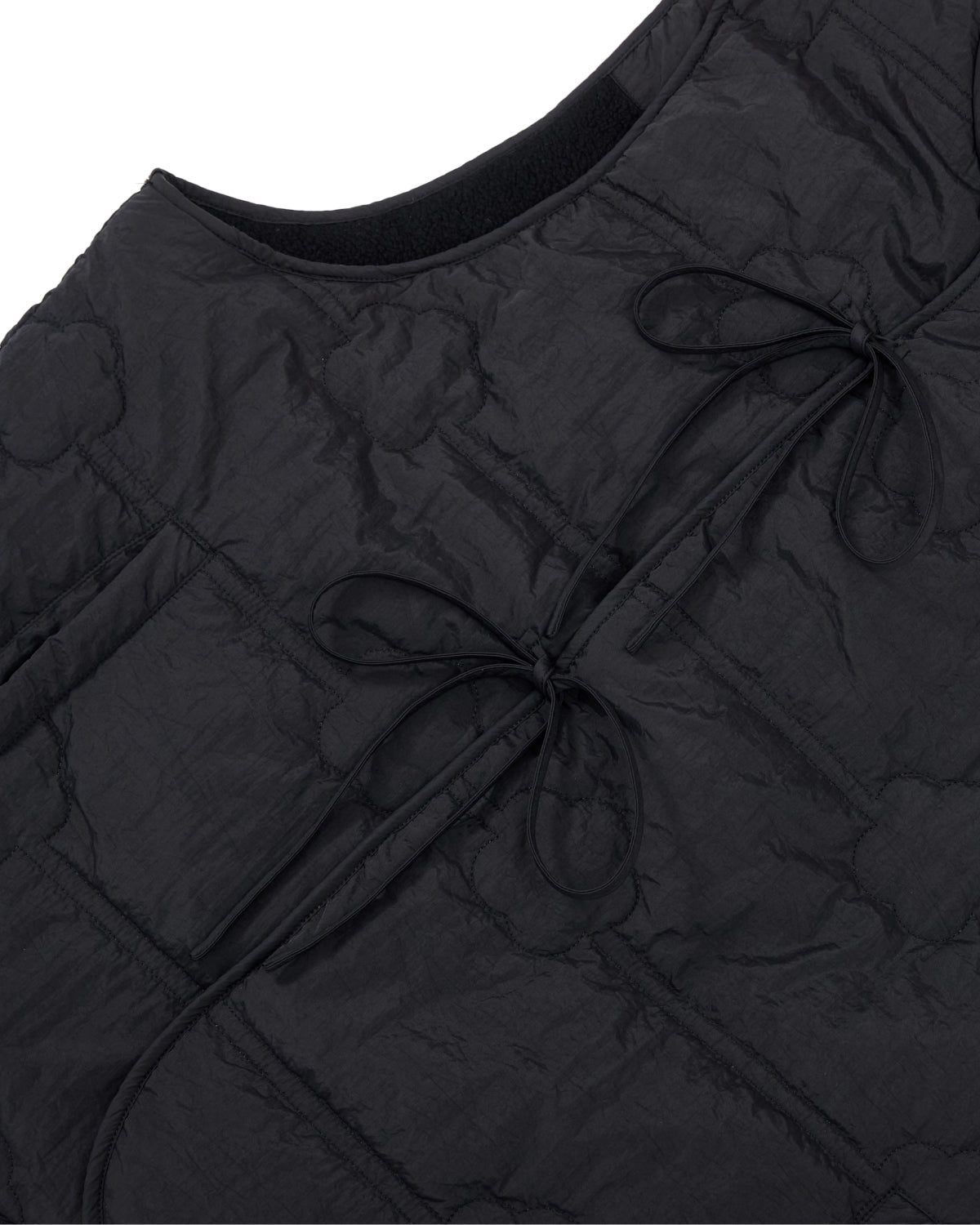 Close-up of the BLACK MOMO REVERSIBLE FLEECE VEST by Sundae School, featuring a black quilted design with two tied bows on the front and a curved neckline. The crinkled fabric showcases visible stitched patterns.
