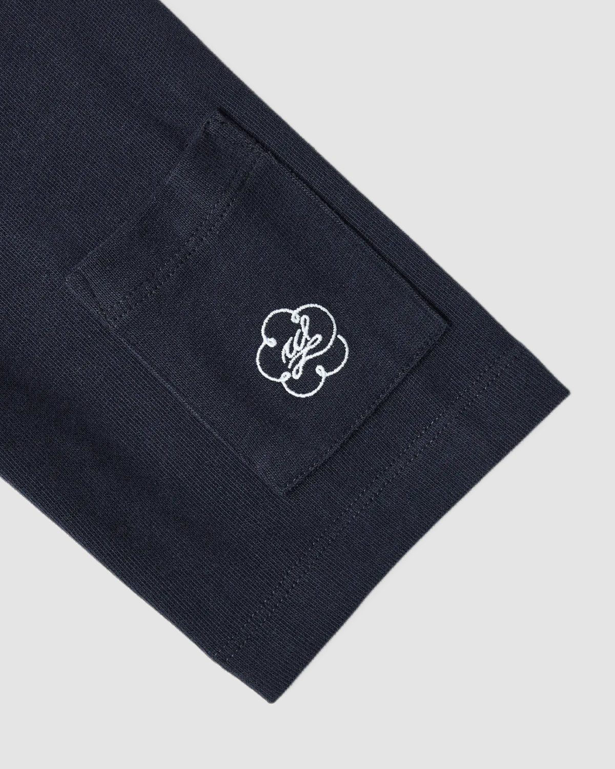 A close-up of the Sundae School NAVY OFFICE QUARTER ZIP shows a dark navy cotton jersey sleeve with a small rectangular stash pocket and a white embroidered cloud-like logo.