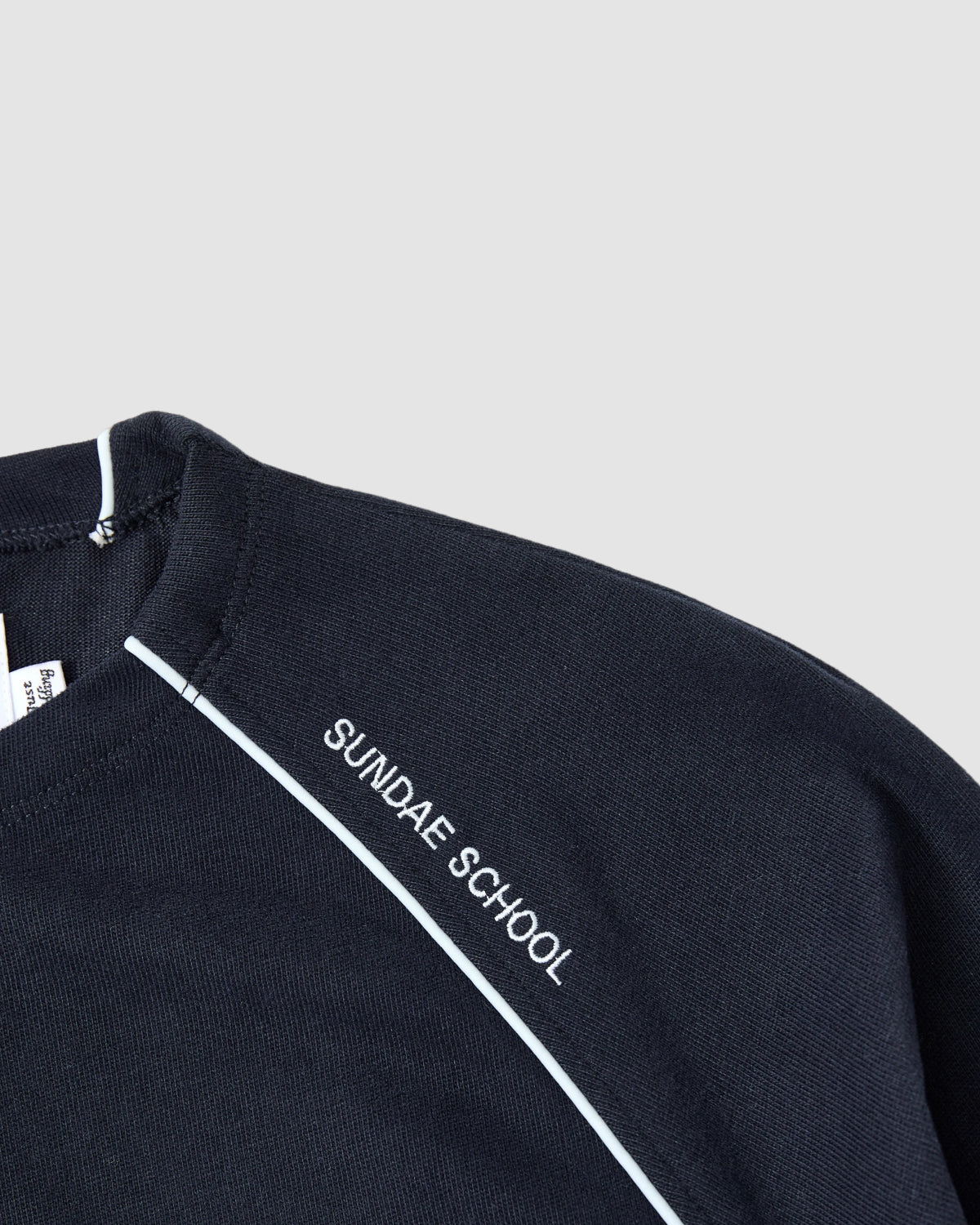 Close-up of the NAVY OFFICE QUARTER ZIP by Sundae School, a navy cotton jersey shirt with “SUNDAE SCHOOL” in white on the shoulder and a white stripe running diagonally across the upper chest and collar.