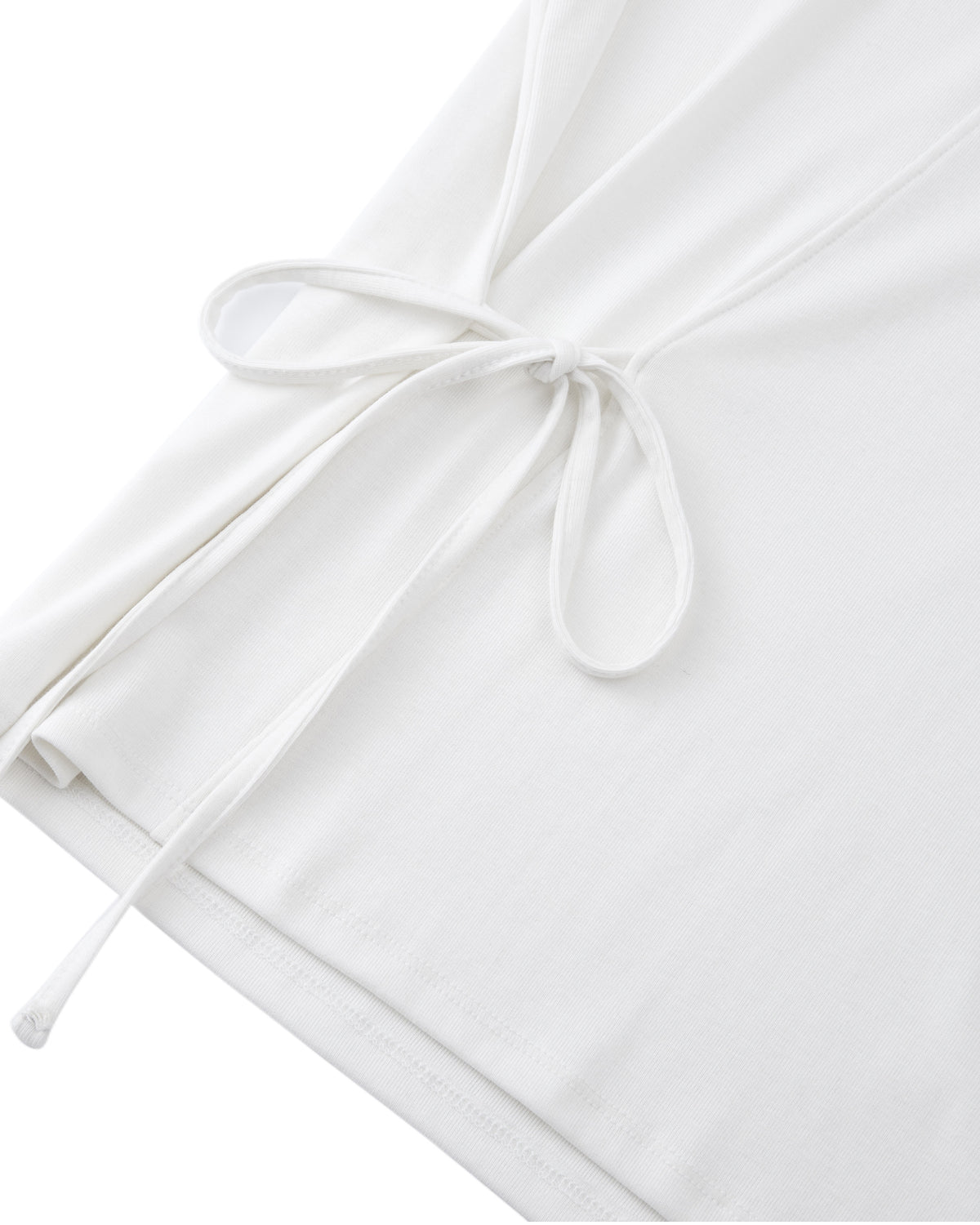 Close-up of the IVORY ORIGAMI GORUM TEE by Sundae School, showcasing a white fabric with a delicate side tie detail. Two strings are knotted into a simple bow, and the material appears soft and lightweight.
