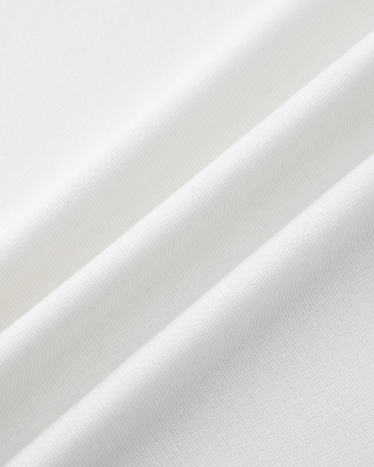 Close-up of the IVORY ORIGAMI GORUM TEE by Sundae School: features white fabric with a soft texture and subtle diagonal folds, revealing fine lines and gentle shadows.