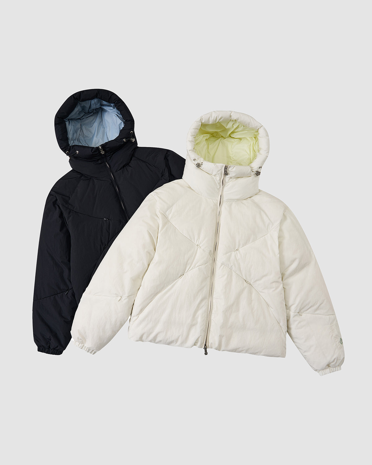 The BLACK SKY BLUE ORIGAMI PUFFER by Sundae School, shown flat in black with blue lining and white with light green lining, both feature hoods and front zippers on a light gray background.
