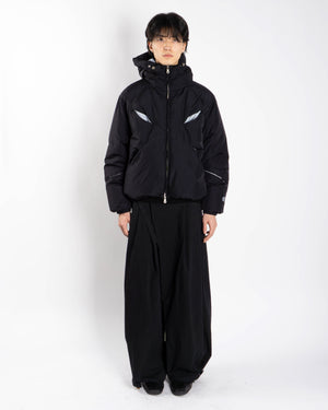 A person stands against a white background wearing the Sundae School BLACK SKY BLUE ORIGAMI PUFFER and wide-legged black pants, facing forward with hands at their sides.