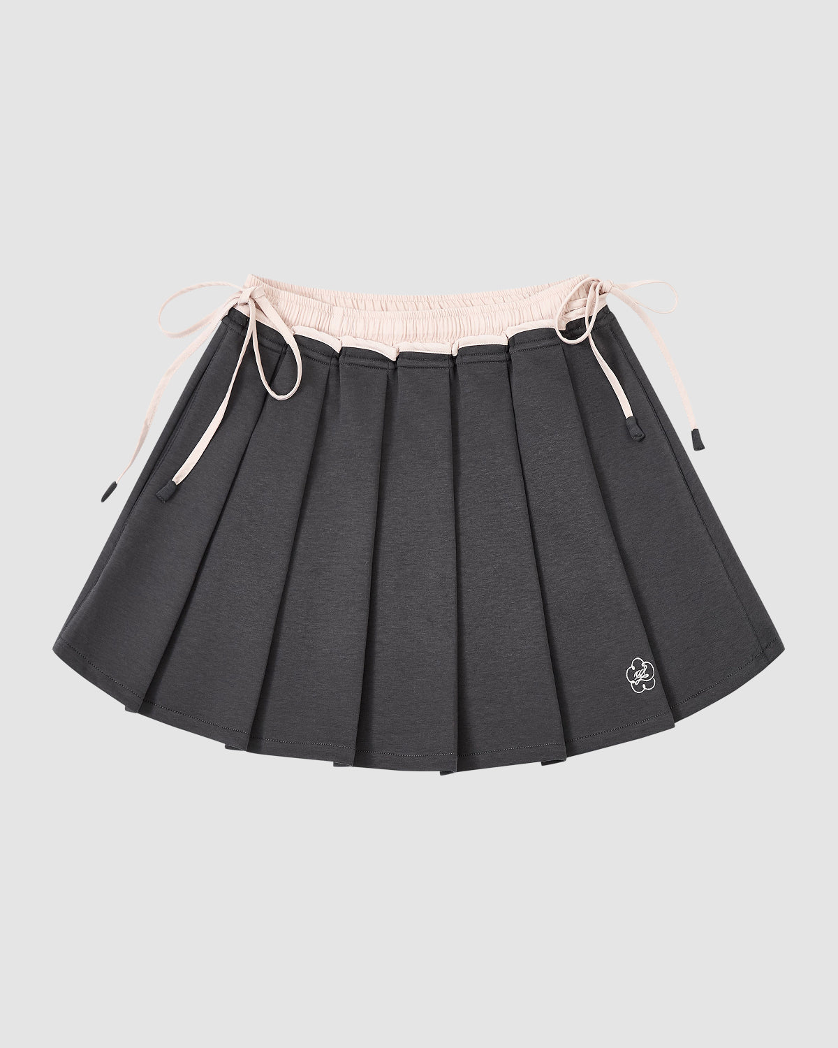 The CHARCOAL PLEATED JERSEY MINI SKIRT by Sundae School features dark gray knife pleats, a light pink elastic waistband with drawstrings, and a small white embroidered flower at the hem, shown against a plain light gray background.