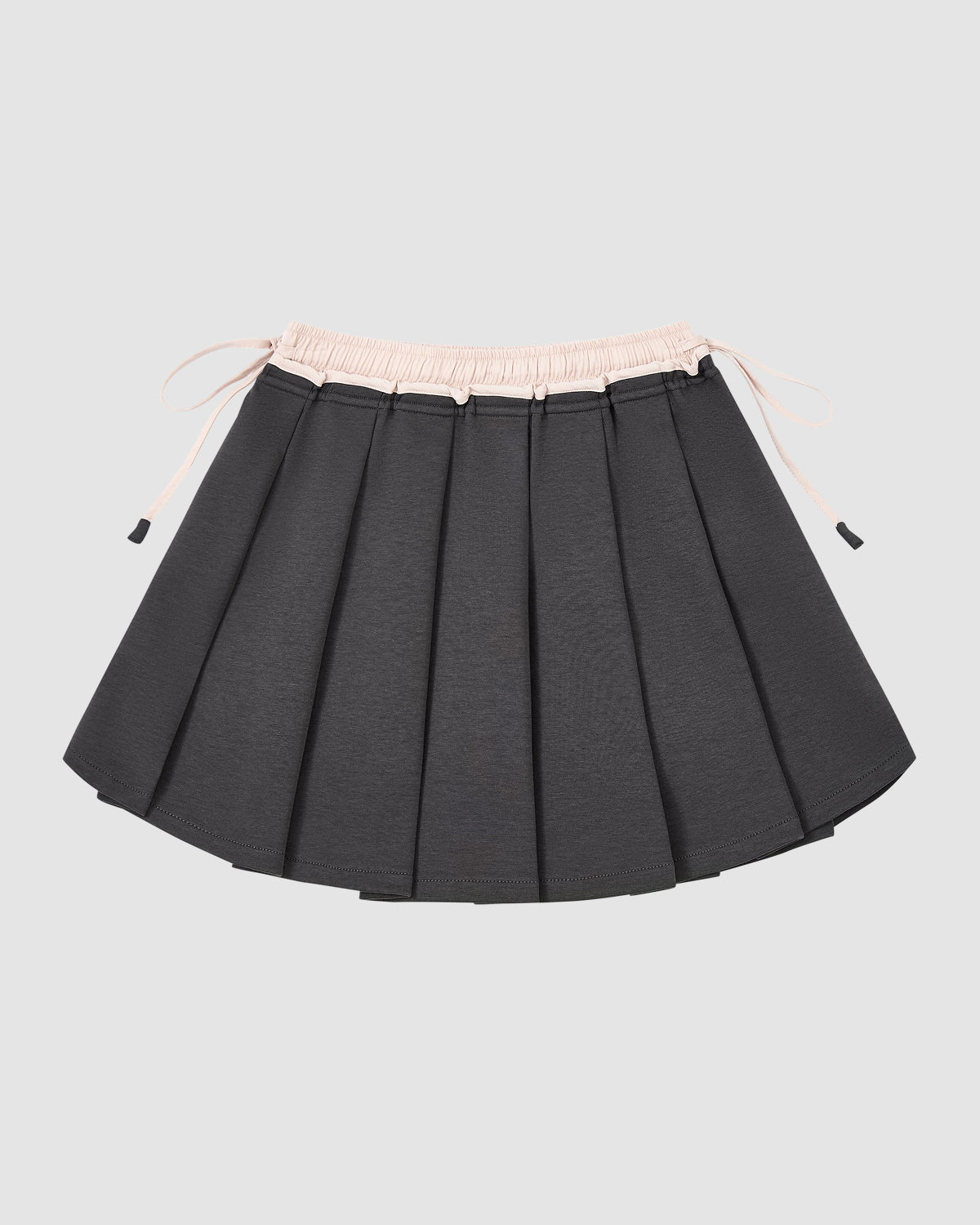 The CHARCOAL PLEATED JERSEY MINI SKIRT by Sundae School features dark gray knife pleats, a light pink elastic waistband with drawstrings, and is displayed against a plain light gray background.