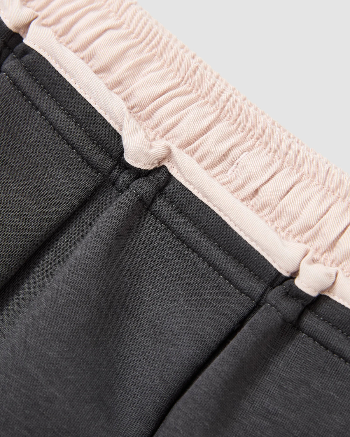 Close-up of the Sundae School CHARCOAL PLEATED JERSEY MINI SKIRT, showcasing a light pink ribbed elastic waistband and dark gray pleated fabric with visible stitching, inspired by the classic schoolgirl skirt style.