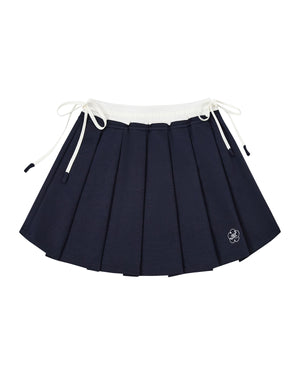 The NAVY PLEATED JERSEY MINI SKIRT by Sundae School features navy blue knife pleats, a white elastic waistband, white drawstrings on each side, and a small embroidered flower near the hem.