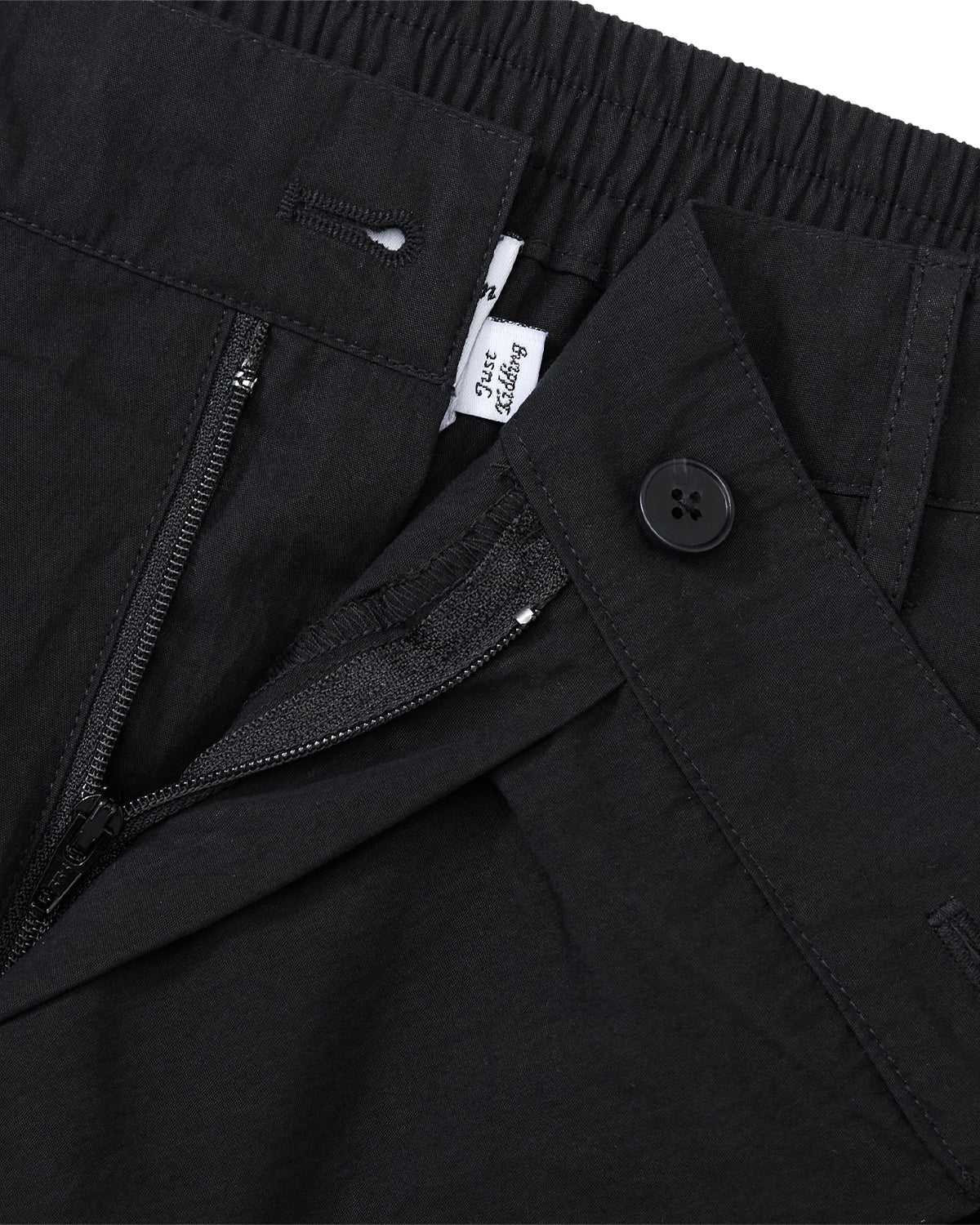 Close-up of Sundae School BLACK PLEATED PALAZZO PANTS with an elastic waistband, zipper fly, black mochi button detail, and a glimpse of a white label featuring black text.