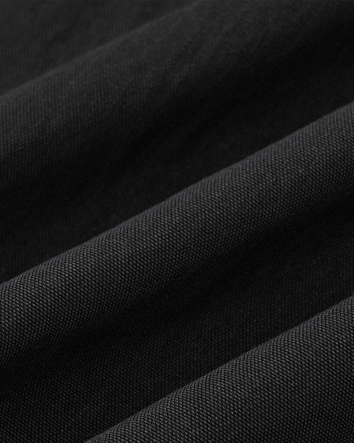 Close-up of black textured fabric from Sundae School's BLACK PLEATED UNIFORM SLACKS, highlighting diagonal pleats and weave details—characteristic of adjustable waist pants in Korean school uniforms.
