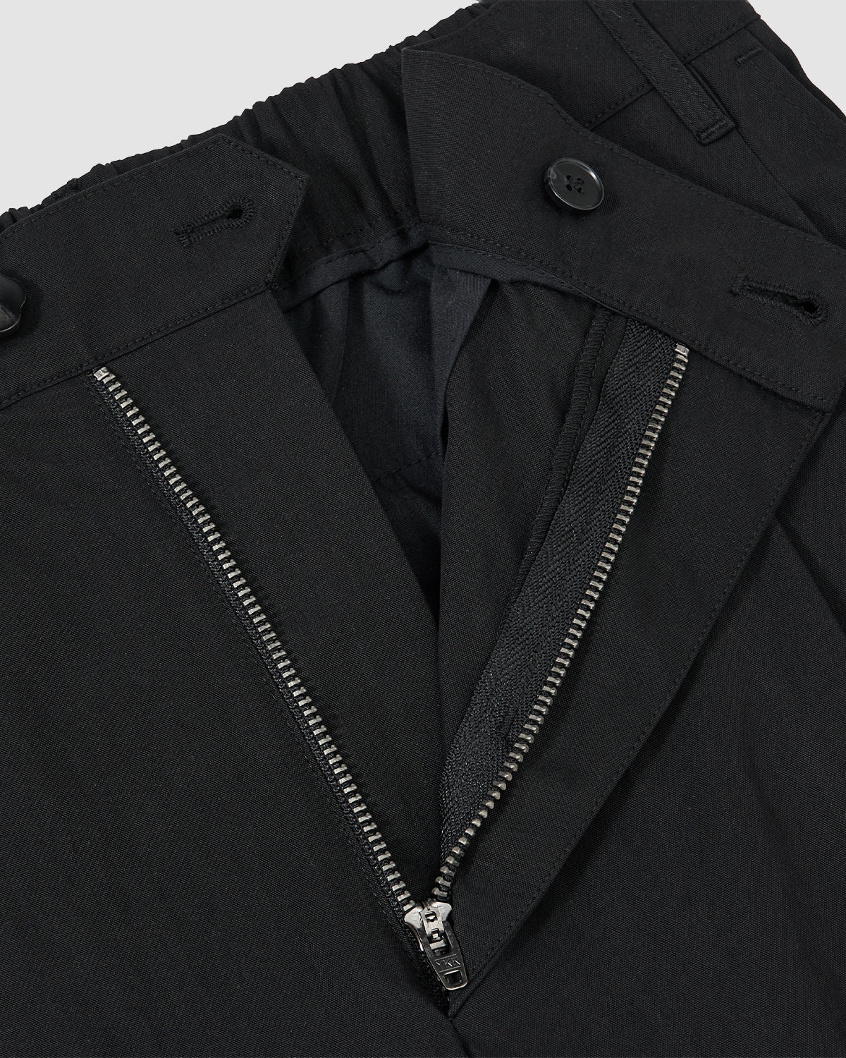 Close-up of Sundae School BLACK PLEATED UNIFORM SLACKS, showing a partially unzipped metal zipper, button closure at the waistband, and visible inner lining with detailed stitching.