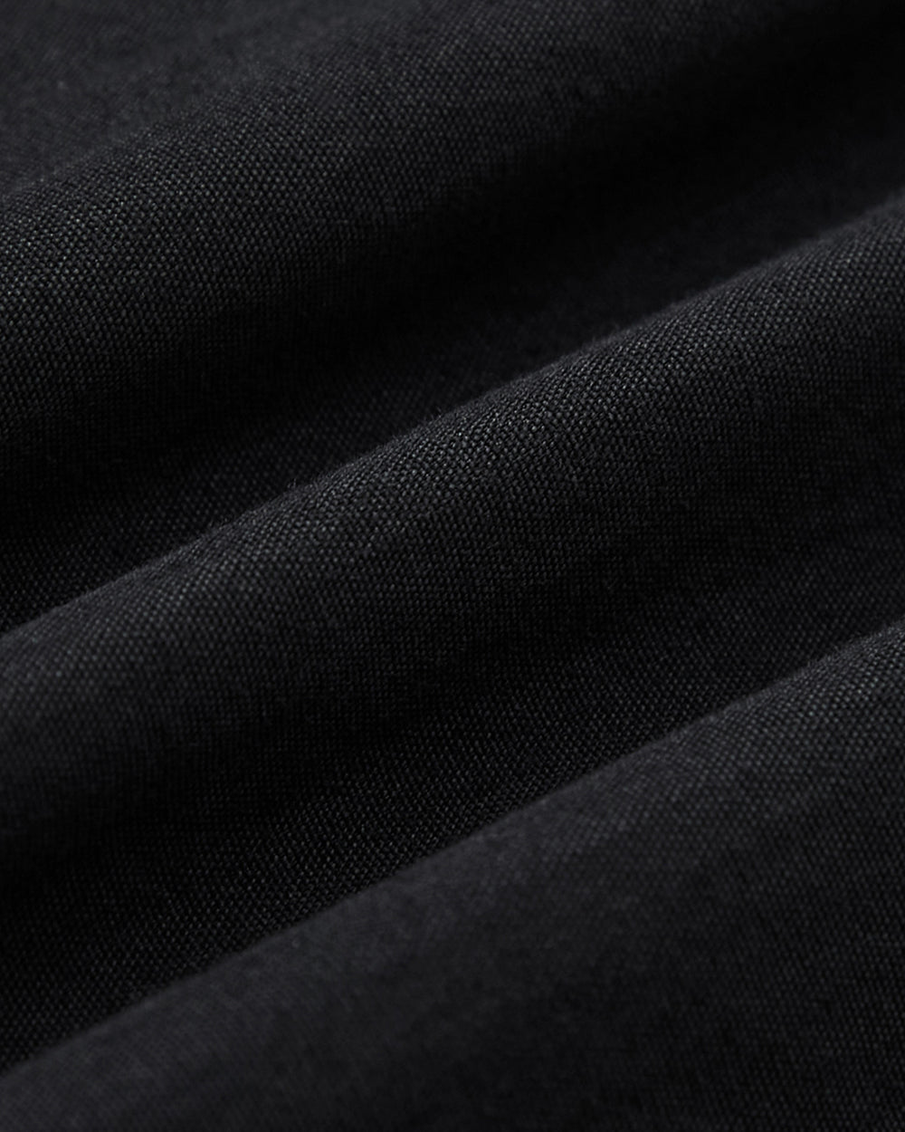 Close-up of black fabric with visible texture and soft folds, highlighting fine woven fibers and gentle shadows—ideal for Sundae School’s BLACK PLEATED PALAZZO PANTS.