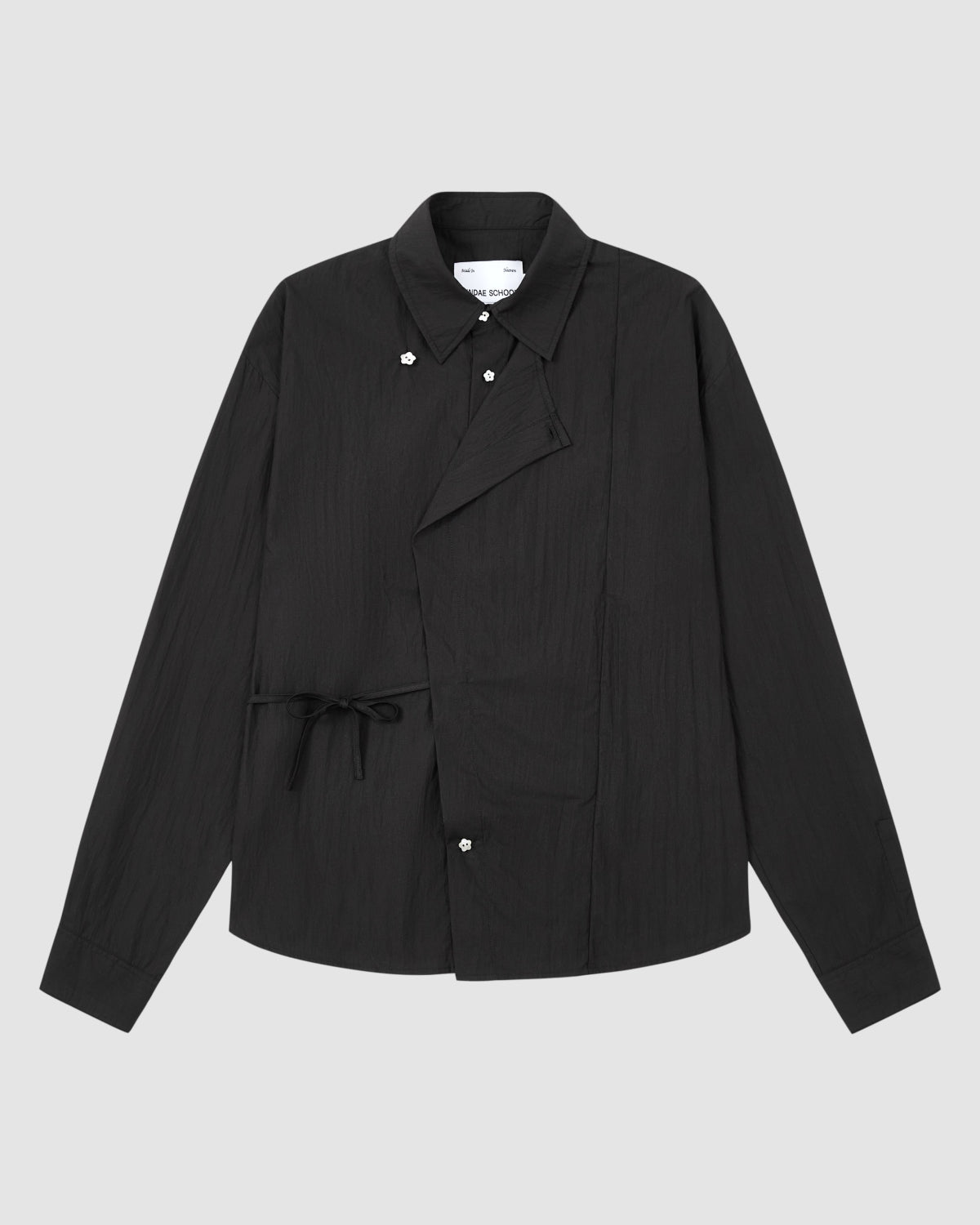 The BLACK POPLIN TIE GORUM SHIRT by Sundae School, featuring long sleeves, an asymmetrical front, button closures, and a side tie detail, is displayed on a plain light grey background.