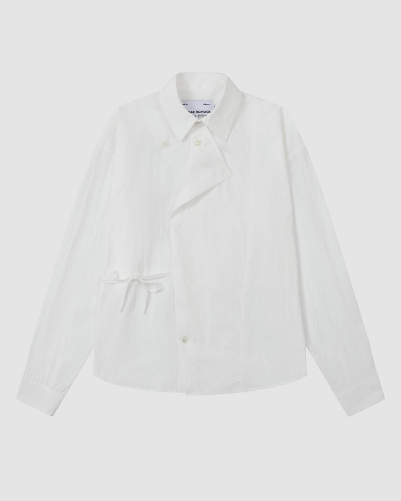 The WHITE POPLIN TIE GORUM SHIRT by Sundae School, a long-sleeve white button-up featuring an asymmetric front and side tie detail, is laid flat on a light background.