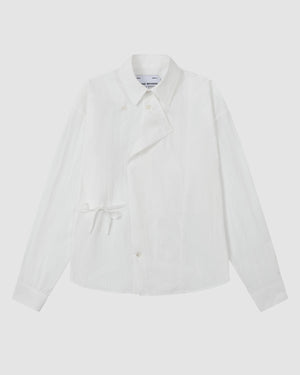The WHITE POPLIN TIE GORUM SHIRT by Sundae School, a long-sleeve white button-up featuring an asymmetric front and side tie detail, is laid flat on a light background.