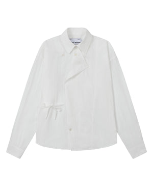 The WHITE POPLIN TIE GORUM SHIRT by Sundae School is a unisex, tailored-fit white long-sleeve shirt crafted from cotton nylon poplin. It features an asymmetrical front, classic collar, and distinctive side tie detail, with a double-layered front panel adding dimension. Shown on a plain background.