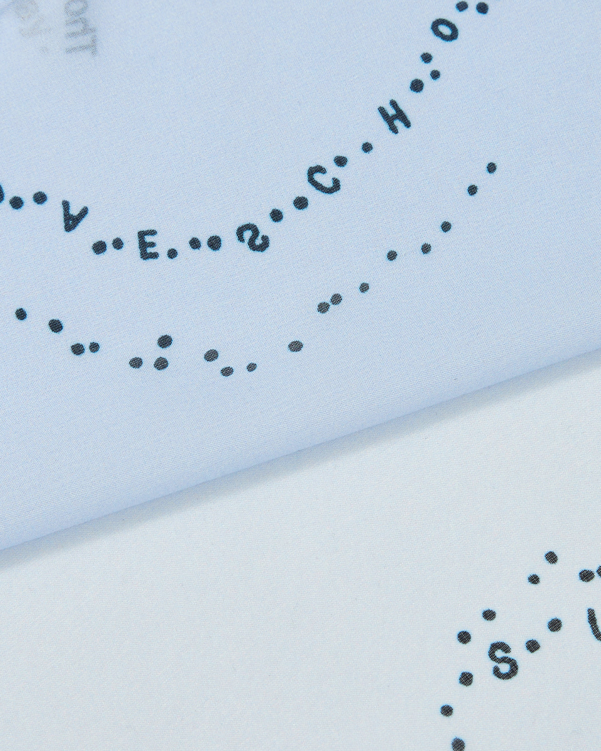 A close-up of black dotted letters forming words in a curved pattern on white organza evokes the delicate texture of Sundae School’s SKY BLUE 10 COMMANDMENTS ORGANZA BANDANA. The design references Sundae School's Ten Commandments collection.