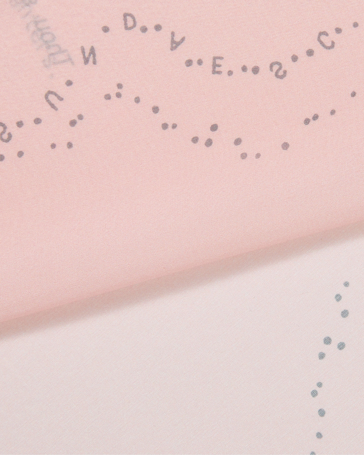 A close-up of Sundae School’s BABY PINK 10 COMMANDMENTS ORGANZA BANDANA shows pink and white silk organza, patterned with small dots and scattered uppercase letters in curving lines, inspired by the Ten Commandments print.